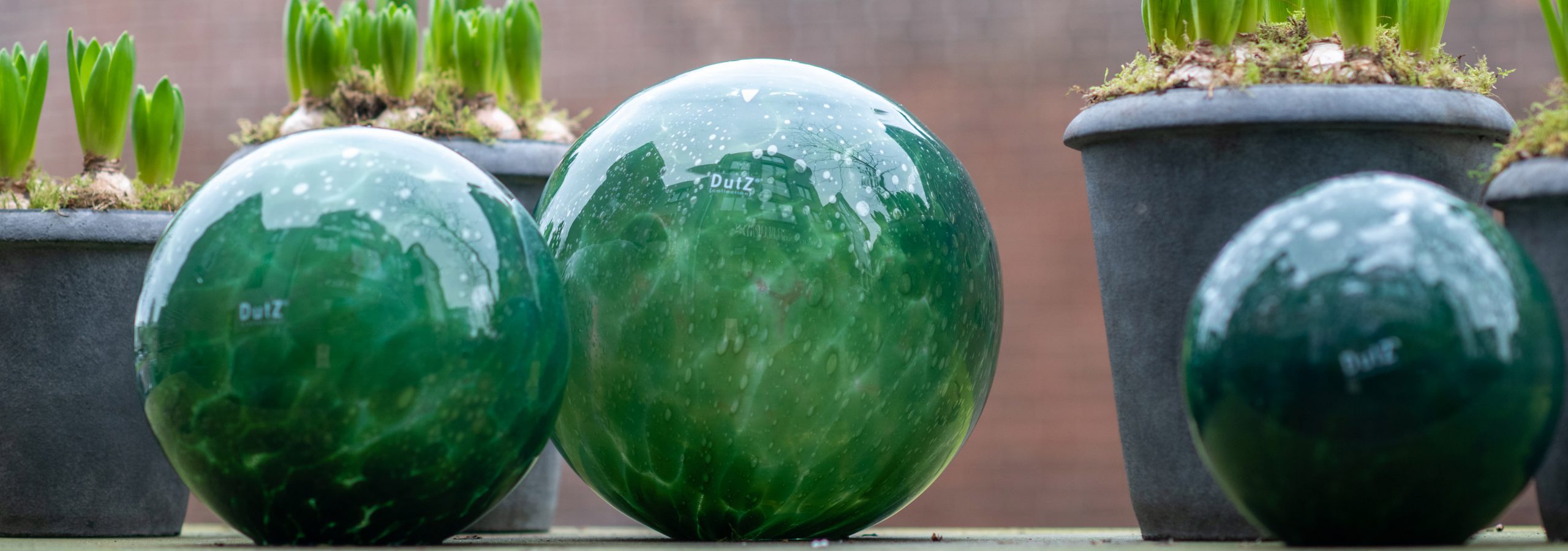 Dutz glazen tuinballen in de kleur donkergroen. Er liggen drie formaten op een tuintafel